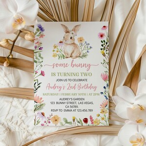 K&ouml;nnte beinhalten: Eine rechteckige Geburtstagseinladungskarte mit einer Aquarellillustration eines braunen Hasen, umgeben von bunten Wildblumen. Der Text lautet: some bunny IS TURNING TWO JOIN US TO CELEBRATE Audrey's 2nd Birthday SATURDAY | FEBRUARY 10TH | AT 2PM AUDREY'S GARDEN 123 BUNNY STREET, LAS VEGAS, CA 56789. RSVP TO EMMA AT 123.456.789