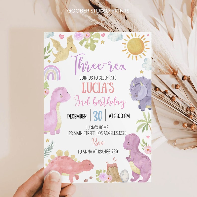 May include: A rectangular birthday invitation card featuring watercolor illustrations of dinosaurs, a volcano, a sun, and a rainbow. The text reads: Three-rex, JOIN US TO CELEBRATE LUCIA'S 3rd birthday, DECEMBER 30 AT 3:00 PM, LUCIA'S HOME 123 MAIN STREET, LOS ANGELES.1235, Rsvp TO ANNA AT 123.456.789.