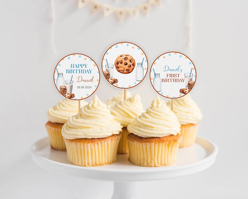 May include: Three round cupcake toppers featuring illustrations of milk bottles, blue striped straws, and chocolate chip cookies. The text reads HAPPY BIRTHDAY Daniel 28.08.202X and Daniel's FIRST BIRTHDAY. The toppers are inserted into frosted cupcakes.