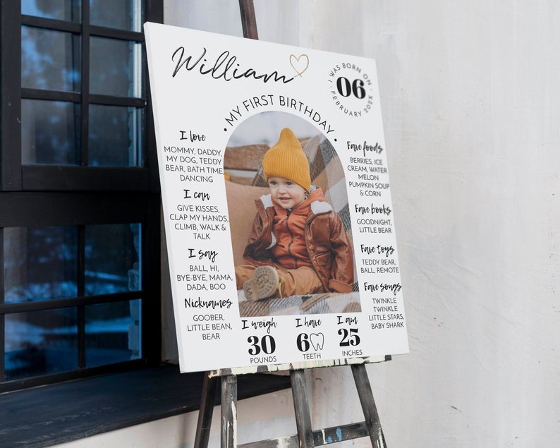 May include: A white sign with a photo of a baby boy in a red hat and brown jacket. The sign says "William, My First Birthday" and lists the baby's favorite foods, books, toys, and songs. It also includes his weight, 30 pounds, number of teeth, 6, and height, 25 inches.