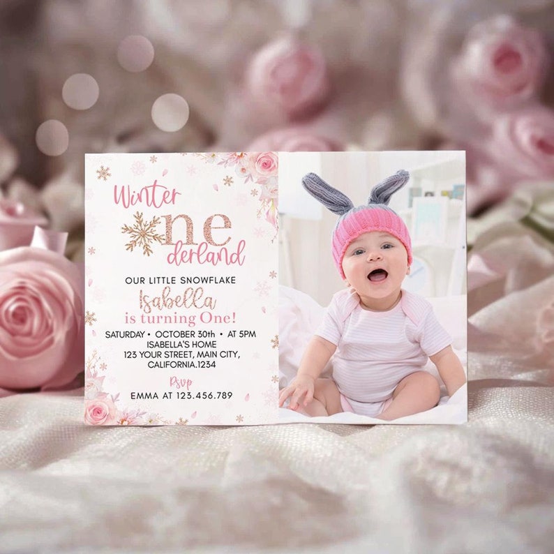 May include: A rectangular birthday invitation card featuring pink roses, gold snowflakes, and the text Winter One-derland. It includes details for Isabella turning one on October 30th at 5 PM, plus a photo of a baby wearing a pink and gray bunny hat.