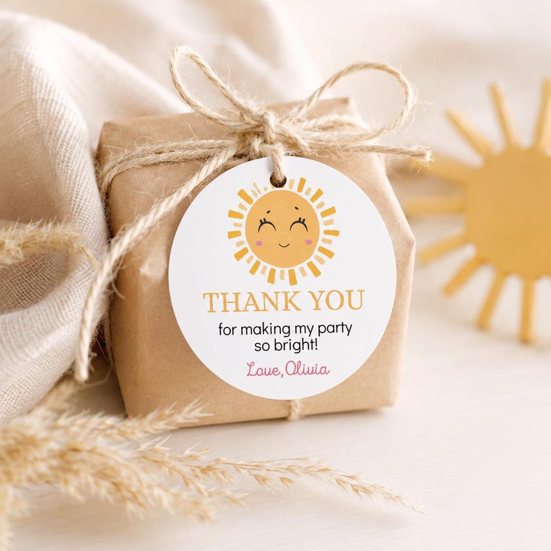 May include: A round white paper gift tag tied with twine to a brown paper wrapped box. The tag features a yellow sun illustration with a smiling face and the text: THANK YOU for making my party so bright! Love, Olivia, in orange and pink.