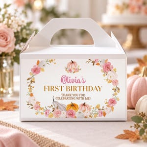 May include: A white cardboard gable box featuring a floral wreath design with pink and white roses, orange and white pumpkins, and the text "Olivia's FIRST BIRTHDAY THANK YOU FOR CELEBRATING WITH ME!" printed in pink and gold on the front panel.