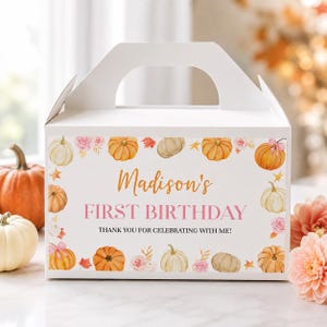 May include: A white cardboard gable box featuring a watercolor print of orange and white pumpkins, pink flowers, and autumn leaves. The text reads: Madison's FIRST BIRTHDAY THANK YOU FOR CELEBRATING WITH ME! The box has a handle at the top.
