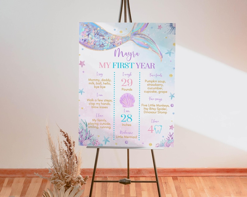 May include: A printable first birthday chart for a baby girl named Mayra. The chart is decorated with a mermaid theme and includes details about her first year, such as her weight, height, and favorite foods. The chart is printed on a white background with a light blue and purple color scheme.
