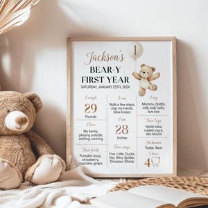 May include: A rectangular framed print titled Jackson's BEAR-Y FIRST YEAR featuring a watercolor teddy bear holding a balloon with the number 1. The poster displays milestones including 29 pounds, 28 inches, favorite foods, songs, and four teeth.