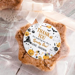 May include: A star-shaped cookie in a clear cellophane bag, tied with a white ribbon. A round tag with Halloween-themed illustrations and the text "THANK YOU for making my day a Spooky One! LOVE, JACKSON" is attached.