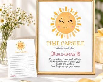 May include: A gold-framed sign and a matching card featuring a smiling yellow sun illustration. The sign reads: TIME CAPSULE To be opened when Olivia turns 18. Please write a message for Olivia. Make a prediction or share your hopes and wishes.