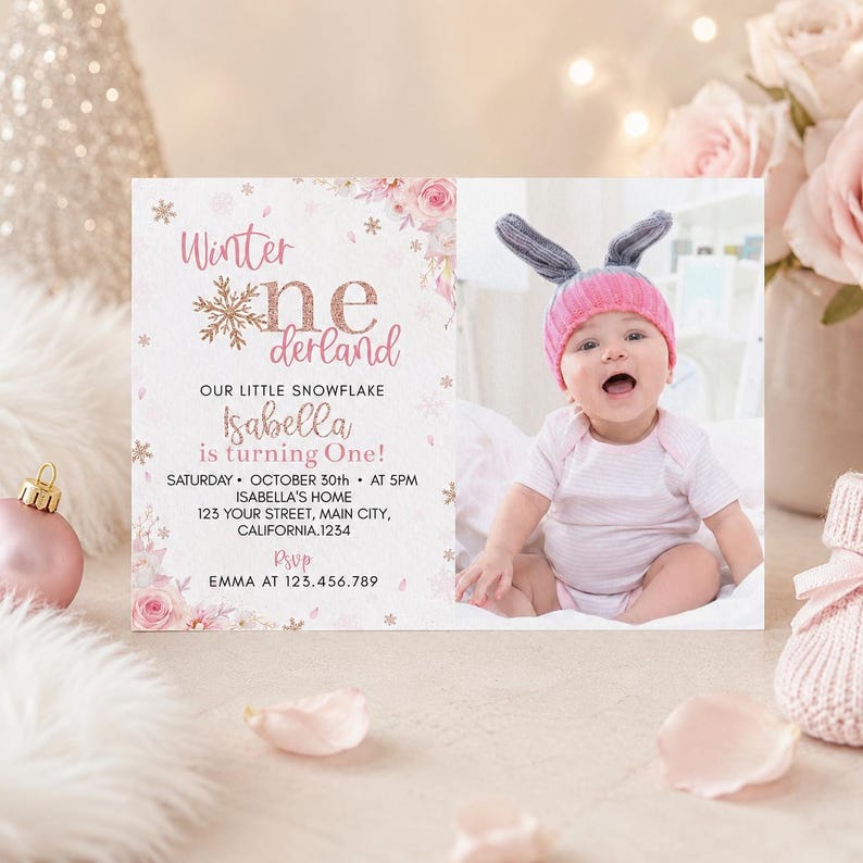 May include: A rectangular invitation card featuring pink floral accents, gold snowflake graphics, and the text Winter onederland. The card includes event details for Isabella's first birthday and a photograph of a baby wearing a pink knit hat.