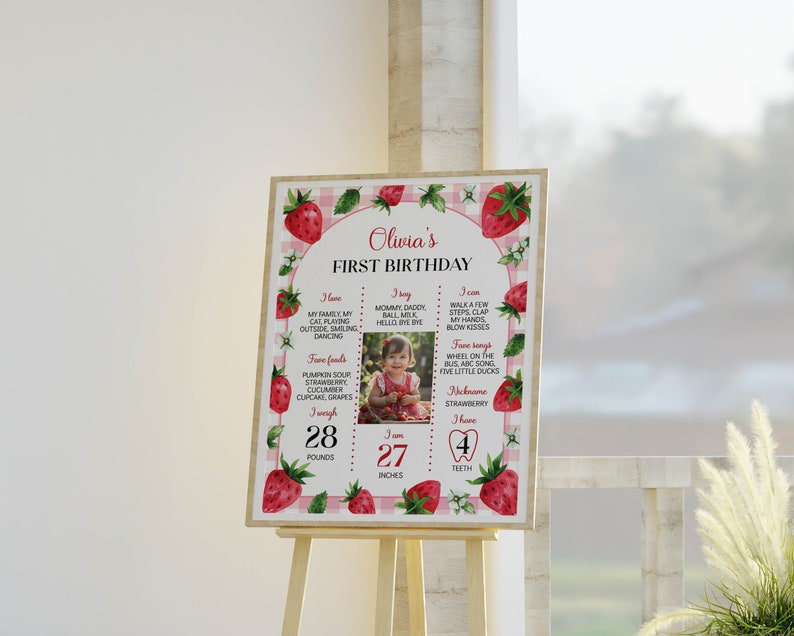May include: A pink and white gingham background with a strawberry border. The center features a photo of a baby girl with a list of milestones for her first birthday. The list includes her weight, height, favorite foods, and things she can do. The text reads "Olivia's First Birthday".