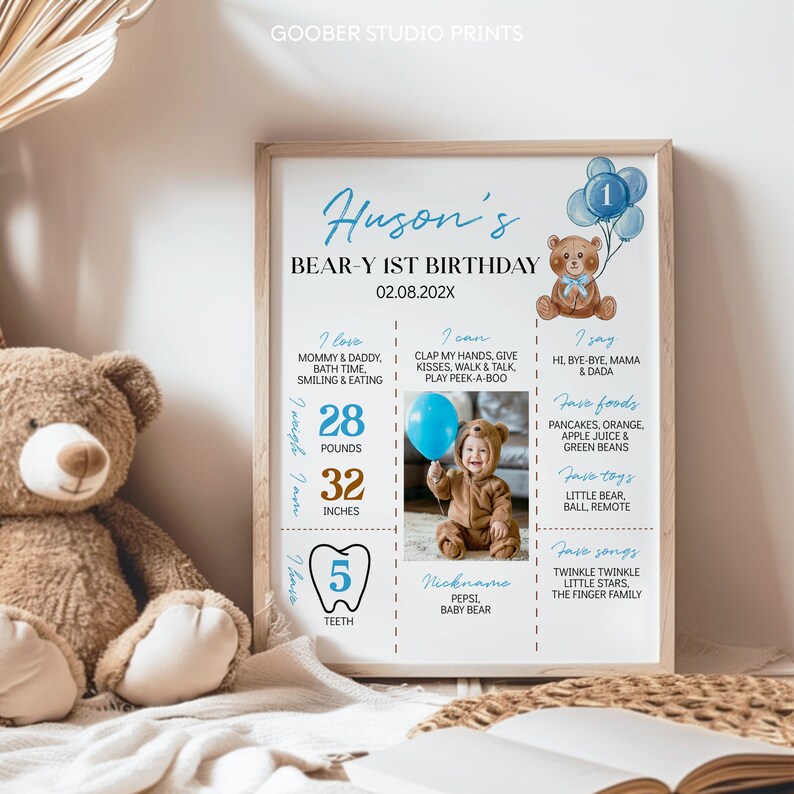 May include: A personalized first birthday milestone poster in a wooden frame featuring a brown teddy bear illustration, blue balloons, and text detailing baby facts including 28 pounds, 32 inches, 5 teeth, and a photo of a child in a bear suit.