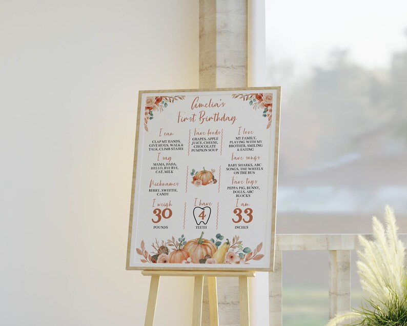 May include: A rectangular milestone birthday sign for Amelia's first birthday, featuring orange and brown pumpkin and floral illustrations. The text lists milestones including I can, fave foods, I love, I say, fave songs, nicknames, fave toys, 30 pounds, 4 teeth, and 33 inches.