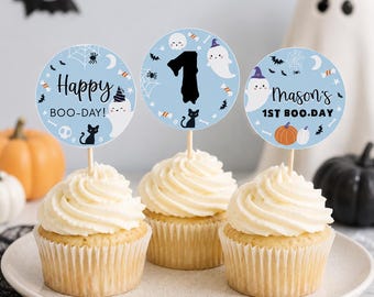 Op de afbeelding: Drie cupcakes met ronde papieren decoraties op stokjes. De ontwerpen hebben lichtblauwe achtergronden met Halloween-motieven zoals spoken, zwarte katten, pompoenen, vleermuizen en spinnenwebben. Tekst: Happy BOO-DAY!, 1, Mason's 1ST BOO.DAY.