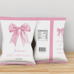 May include: Two white snack bags with pink trim featuring a large pink bow illustration. The front displays "Juliana's FIRST BIRTHDAY" and "25.11.202X". The back includes a "NUTRITION FACTS" label, a barcode, and the text "Thank you for celebrating with me".