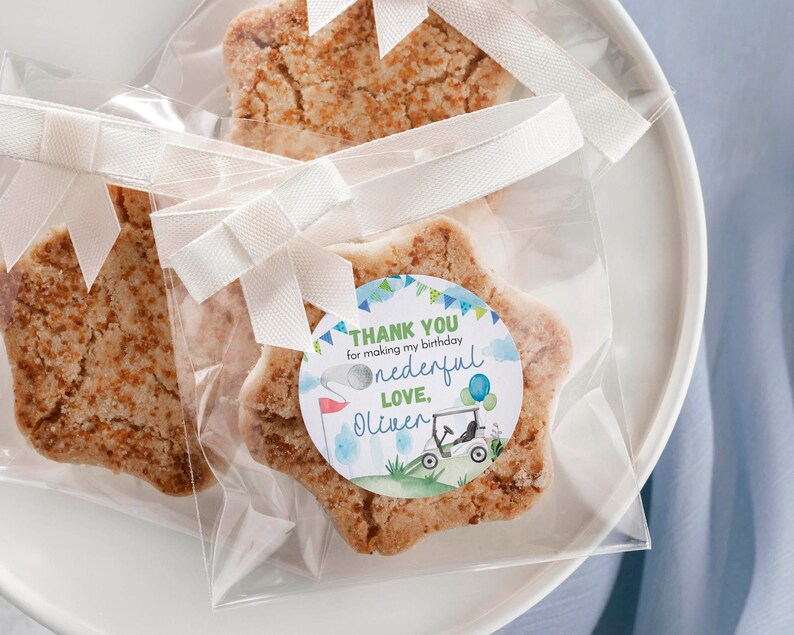 May include: Star-shaped sugar cookies with a golden-brown textured surface, each individually wrapped in clear plastic bags tied with white ribbon. A circular sticker on the front reads: THANK YOU for making my birthday onederful LOVE, Oliver.