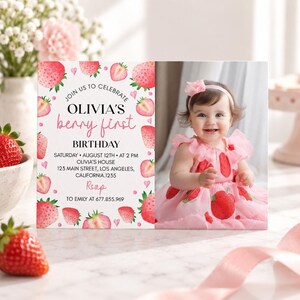 May include: A rectangular birthday invitation card featuring a white background with watercolor strawberry illustrations and pink text. The card reads: JOIN US TO CELEBRATE OLIVIA'S berry first BIRTHDAY, SATURDAY AUGUST 12TH AT 2 PM, OLIVIA'S HOUSE, 123 MAIN STREET, LOS ANGELES, CALIFORNIA 1235, RSVP TO EMILY AT 677.855.969. A photograph of a smiling child wearing a pink strawberry-patterned dress and a matching headband is on the right side.