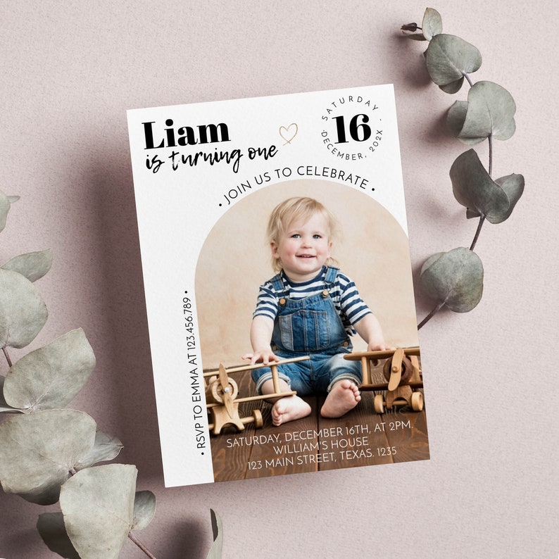 May include: A rectangular birthday invitation card featuring a photo of a child in blue denim overalls and a striped shirt sitting with wooden toy airplanes. The text reads Liam is turning one, Saturday December 16, 202X, and event details.