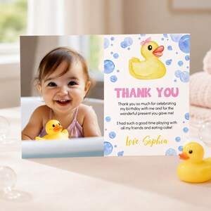 May include: A rectangular thank you card featuring a photo of a smiling child holding a yellow rubber duck on the left and a white background with blue bubbles, a yellow rubber duck illustration, and text on the right side reading Thank You.