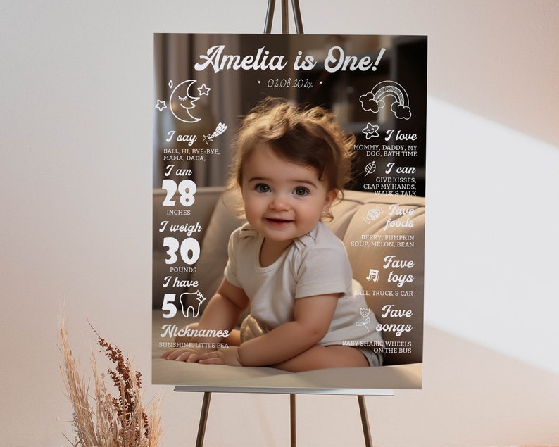 May include: A milestone birthday sign featuring a photograph of a child and white text on a dark background. The text includes Amelia is One, 28 inches, 30 pounds, 5 teeth, and lists of favorite foods, toys, and songs alongside various line art icons.