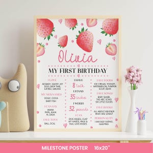 Pode incluir: Um cartaz de marcos em uma moldura de madeira clara com tema de morango, cora&ccedil;&otilde;es e pontos rosa. O texto diz Olivia My First Birthday, listando detalhes pessoais incluindo 8 dentes, 35 polegadas e 32 libras, com comidas, m&uacute;sicas e brinquedos favoritos.