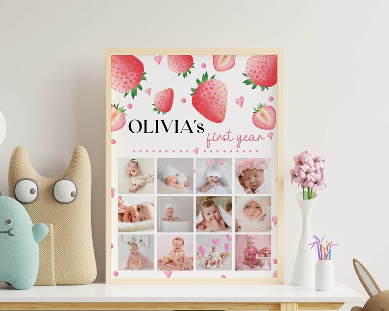 K&ouml;nnte beinhalten: Ein rechteckiges Poster in einem hellen Holzrahmen mit dem Text OLIVIA'S first year. Das Design enth&auml;lt Aquarell-Erdbeerillustrationen und kleine rosa Herzen sowie ein Raster aus zw&ouml;lf Fotos, die die Meilensteine eines Babys zeigen.