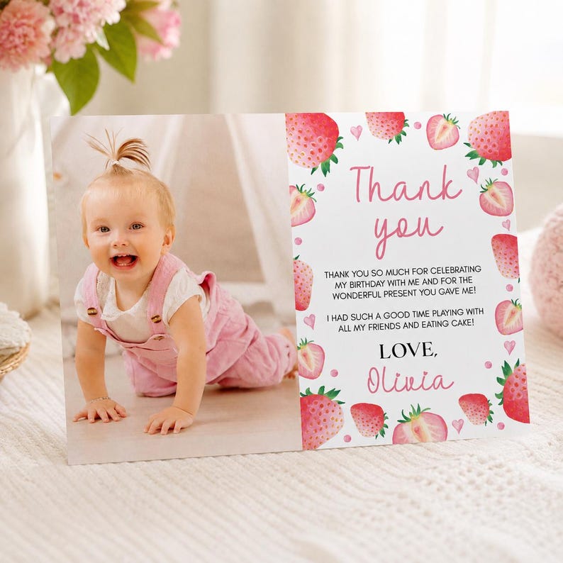 May include: A rectangular thank you card featuring a photo of a baby in pink overalls on the left and a white background with strawberry illustrations and pink text on the right. The text reads: Thank you, Thank you so much for celebrating my birthday with me and for the wonderful present you gave me! I had such a good time playing with all my friends and eating cake! Love, Olivia.