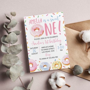 May include: A rectangular birthday invitation card featuring a pink frosted donut and colorful sprinkles. The text reads: AMELIA is a sweet ONE! PLEASE JOIN US TO CELEBRATE Amelia's 1st birthday SATURDAY 26 AUGUST AMELIA'S HOME 123 MAIN STREET, LAS VEGAS. 1235 AT 3:00 PM RSVP TO ANNA AT 123.456.789.