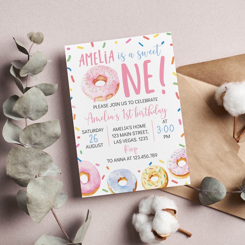 May include: A rectangular birthday invitation card featuring a pink frosted donut and colorful sprinkles. The text reads: AMELIA is a sweet ONE! PLEASE JOIN US TO CELEBRATE Amelia's 1st birthday SATURDAY 26 AUGUST AMELIA'S HOME 123 MAIN STREET, LAS VEGAS. 1235 AT 3:00 PM RSVP TO ANNA AT 123.456.789.