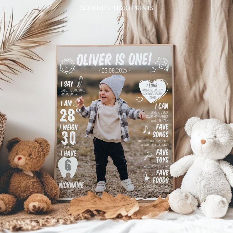 May include: A personalized milestone poster titled OLIVER IS ONE! featuring a central photograph of a toddler in a grey beanie, plaid shirt, and dark pants. The poster includes white text detailing stats like 28 inches, 30 pounds, 6 teeth, and favorite songs, toys, and foods.