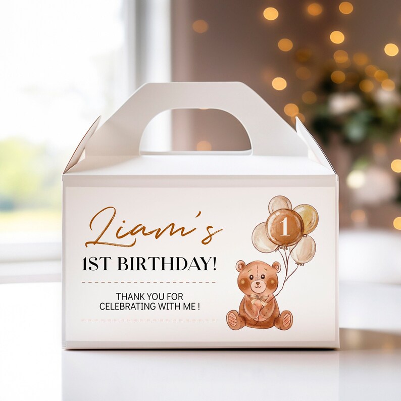 May include: A white cardboard gable box featuring a printed design with the text Liam's 1ST BIRTHDAY! THANK YOU FOR CELEBRATING WITH ME! and a watercolour illustration of a brown teddy bear holding a cluster of balloons with the number 1.