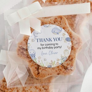 May include: A star-shaped cookie in a clear cellophane bag, tied with a white ribbon and bow. A circular sticker reads "THANK YOU for coming to my birthday party! Love, Oliver" with sea creature illustrations.