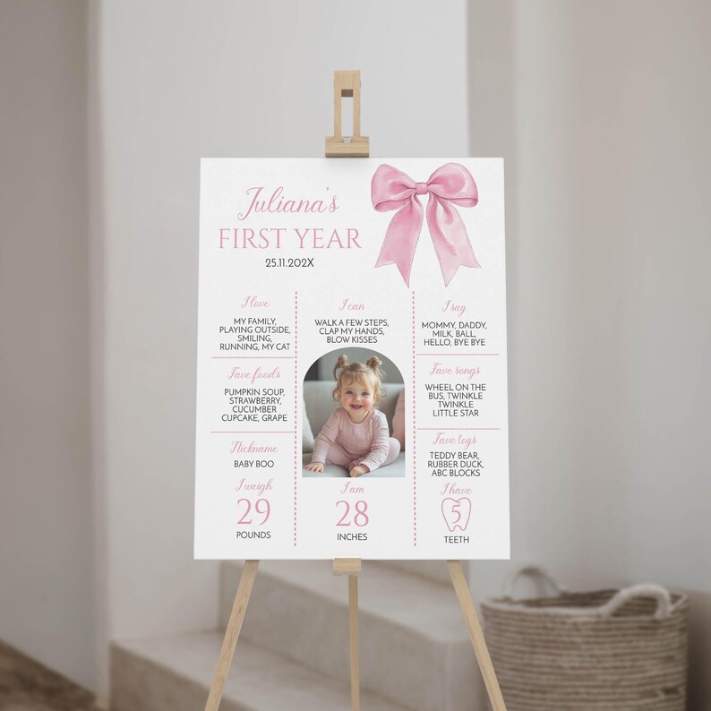 May include: A pink and white first year milestone poster with a watercolor bow at the top. The poster includes information about the baby's first year, including their weight, height, favorite foods, and activities. The poster also includes a photo of the baby.