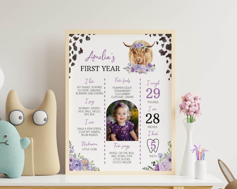 May include: A rectangular milestone poster titled Amelia's First Year featuring a highland cow illustration with purple flowers, cow print corners, and text detailing favorite foods, songs, and physical stats like 29 pounds and 28 inches.