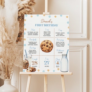 May include: A blue and gold first birthday chart for a boy named Daniel. The chart lists his favorite foods, toys, songs, and things he can do. It also includes his weight, height, and number of teeth. The chart is decorated with cookies and a glass of milk.