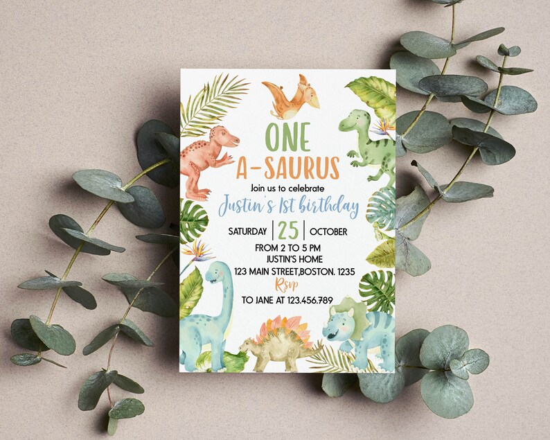Op de afbeelding: Een rechthoekige verjaardagsuitnodigingskaart met aquarelillustraties van verschillende dinosaurussen en tropische bladeren. De tekst luidt: ONE A-SAURUS, Join us to celebrate Justin's 1st birthday, SATURDAY 25 OCTOBER, FROM 2 TO 5 PM, JUSTIN'S HOME, 123 MAIN STREET, BOSTON. 1235, RSVP TO JANE AT 123.456.789.