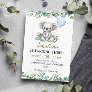 May include: A rectangular birthday invitation card featuring a watercolor illustration of a koala holding a light blue balloon with the number 3. The text reads: Jonathan IS TURNING THREE! AUGUST 28 AT 2PM JONATHAN'S HOUSE 123 MAIN STREET, LAS VEGAS. 1235 RSVP TO JESSICA AT 123.456.789.