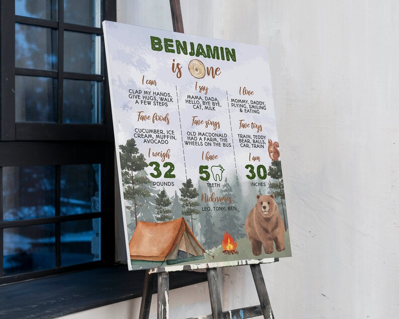May include: A rectangular milestone birthday sign for a one-year-old named Benjamin, featuring a forest theme with a brown bear, a tent, and a campfire. The text details personal milestones, including weight of 32 pounds and height of 30 inches.