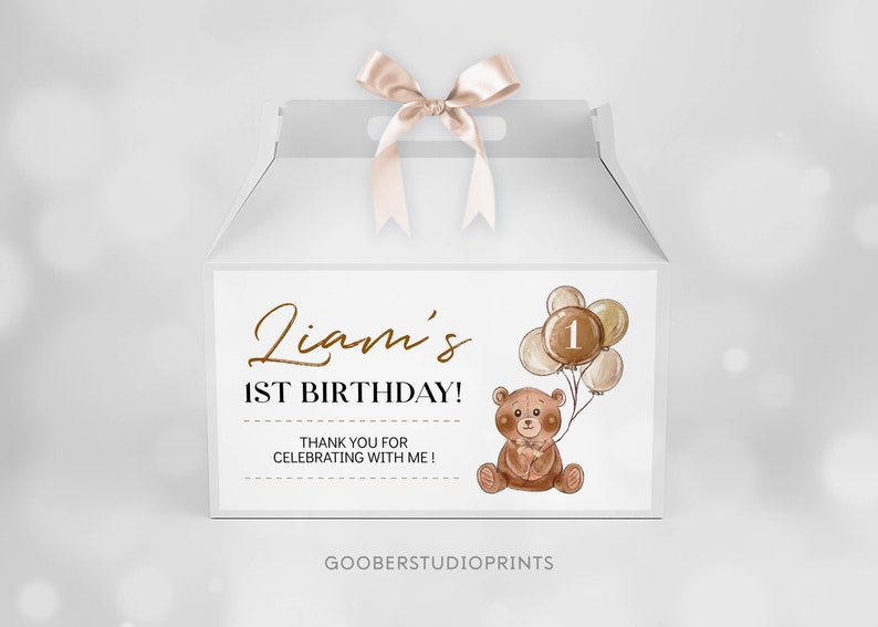 May include: A white gable box with a satin ribbon bow on top, featuring a printed label that reads Liam's 1ST BIRTHDAY! THANK YOU FOR CELEBRATING WITH ME! The design includes a brown teddy bear holding a cluster of balloons with the number 1.