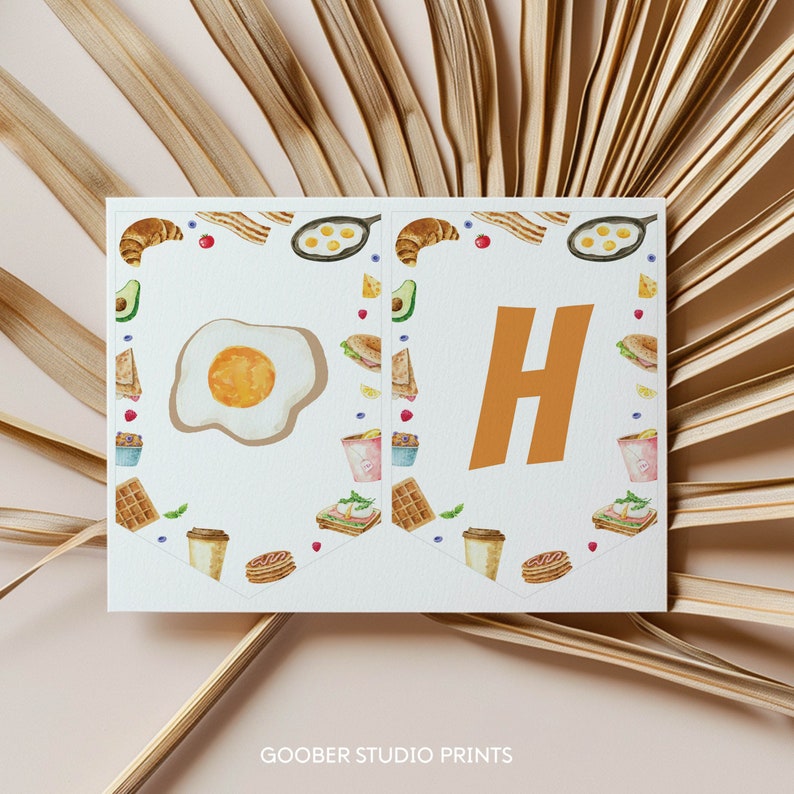May include: A printable banner with a breakfast theme. The banner features the letters "OH" in orange with a white background. The letters are surrounded by a border of breakfast foods, including eggs, bacon, waffles, and coffee.