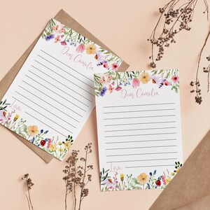 May include: Two white stationery sheets with horizontal black lines, featuring watercolor floral borders in pink, yellow, blue, and green. The text "Dear Camelia" is printed at the top, and the word "Love" is printed at the bottom of each sheet.