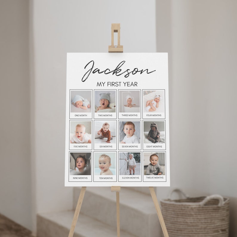 Op de afbeelding: Een wit rechthoekig bord met de titel Jackson My First Year met twaalf individuele vierkante foto's van een baby, elk gelabeld met een maand van &eacute;&eacute;n tot twaalf. Het bord wordt weergegeven op een lichte houten ezelstandaard.