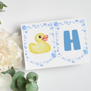 Puede incluir: Una pieza de banner rectangular blanca que presenta un pato de goma amarillo en acuarela a la izquierda y una letra H azul grande a la derecha, ambos rodeados por un borde de burbujas azul claro de varios tama&ntilde;os.