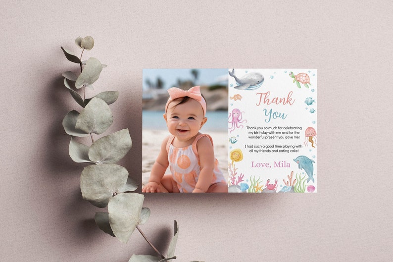 May include: A rectangular thank you card featuring a photograph of a smiling baby on a beach on the left side. The right side displays watercolor illustrations of sea creatures and the text: Thank You, Thank you so much for celebrating my birthday with me and for the wonderful present you gave me! I had such a good time playing with all my friends and eating cake! Love, Mila.