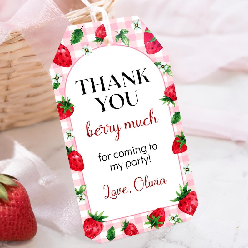May include: A rectangular gift tag with a pink and white gingham border featuring watercolor strawberries and white flowers. The text reads: THANK YOU berry much for coming to my party! Love, Olivia. A white string is attached to the top.