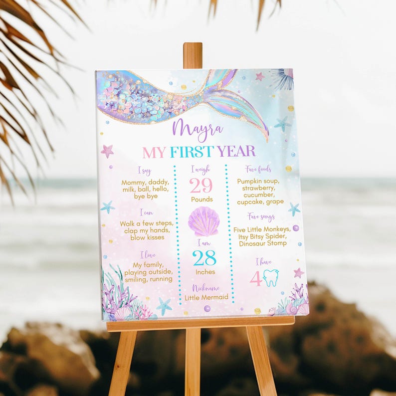 May include: A pastel blue and pink first birthday milestone poster with a mermaid tail design. The poster features the name "Mayra" and details about her first year, including her weight, height, favorite foods, and songs.