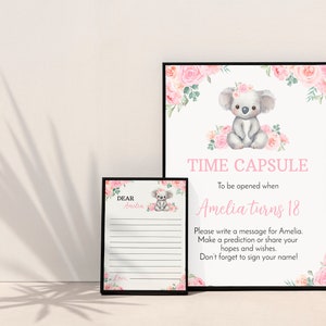 K&ouml;nnte beinhalten: Ein Zeitkapsel-Schild und eine passende Nachrichtenkarte in schwarzen Rahmen. Das Schild zeigt einen Aquarell-Koala mit rosa Blumen und den Text: TIME CAPSULE To be opened when Amelia turns 18. Die Karte tr&auml;gt die Aufschrift: DEAR Amelia, mit Zeilen.
