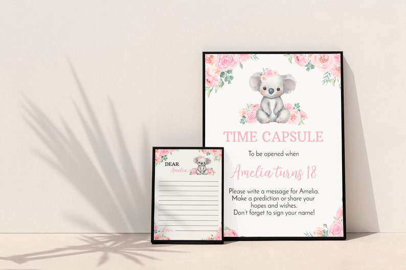 K&ouml;nnte beinhalten: Ein Zeitkapsel-Schild und eine passende Nachrichtenkarte in schwarzen Rahmen. Das Schild zeigt einen Aquarell-Koala mit rosa Blumen und den Text: TIME CAPSULE To be opened when Amelia turns 18. Die Karte tr&auml;gt die Aufschrift: DEAR Amelia, mit Zeilen.