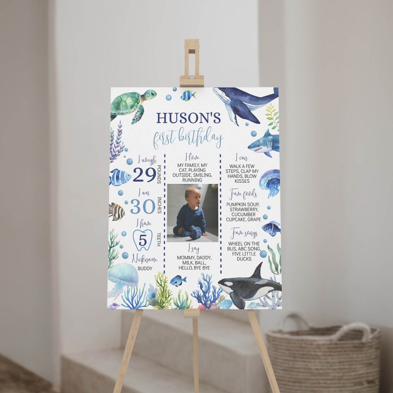 May include: A blue and white first birthday milestone poster with a photo of a baby boy. The poster features a watercolor illustration of sea creatures, including a whale, a turtle, and jellyfish. The poster includes the baby's name, Huson, and details about his first year, including his weight, height, and favorite foods and songs.