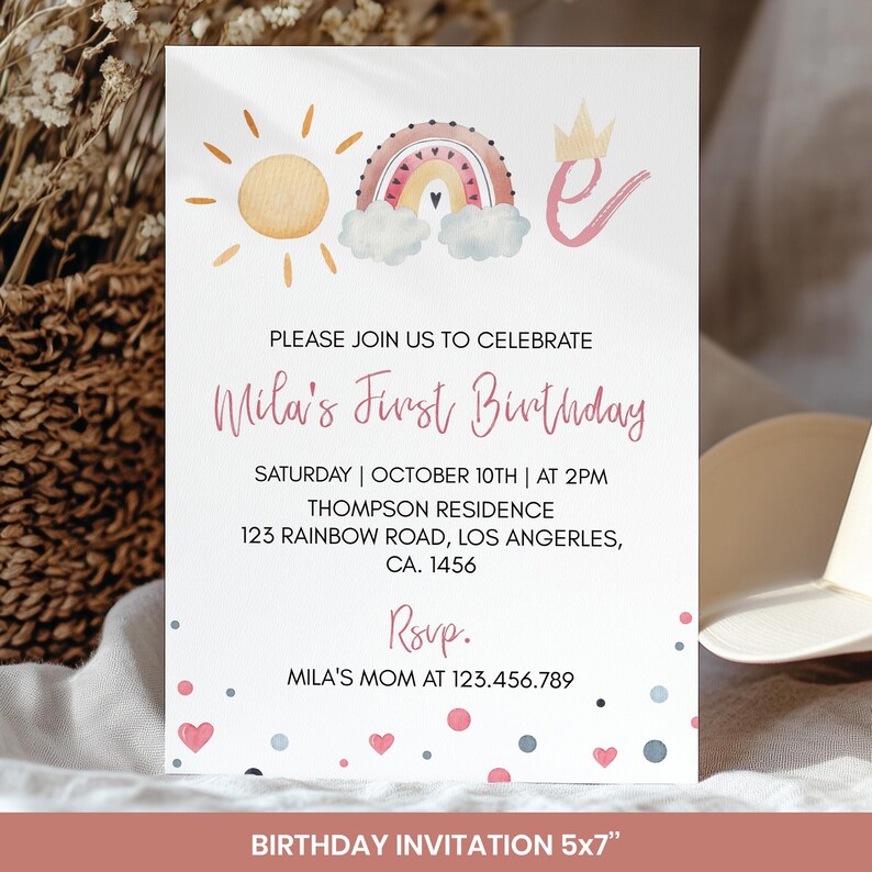 May include: A white birthday invitation featuring a watercolour rainbow, sun, and crown design. The invitation reads "Mila's First Birthday" with event details. The invitation is 12.7 x 17.8 cm.