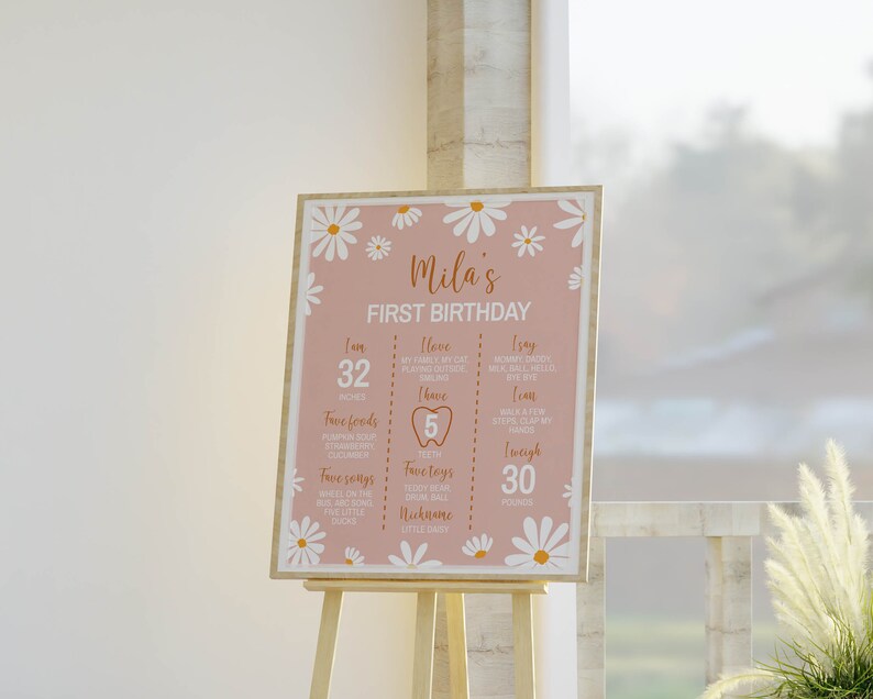 May include: A pink and white first birthday sign with daisies and the text "Mila's First Birthday". The sign lists the child's age, height, weight, favorite foods, songs, toys, and nickname.